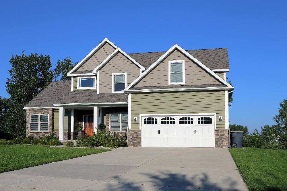 Two-story suburban home with brick and siding exterior, white garage doors, front porch, and manicured lawn