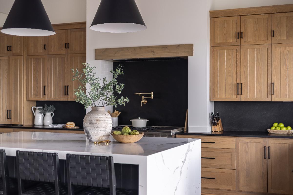 Modern kitchen with marble island, wood cabinets, black backsplash and pendant lights