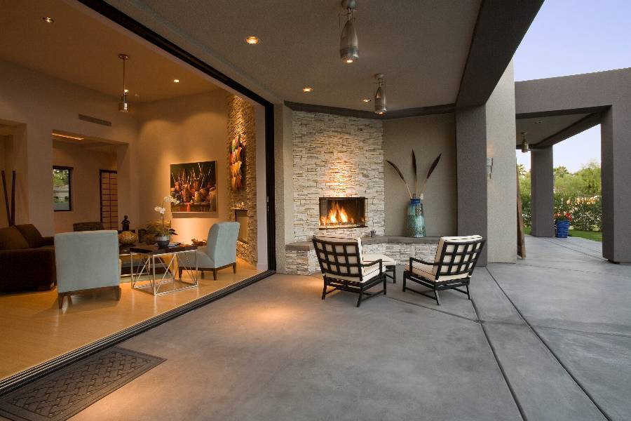 Modern home exterior with fireplace, seating areas, and large glass sliding doors overlooking patio