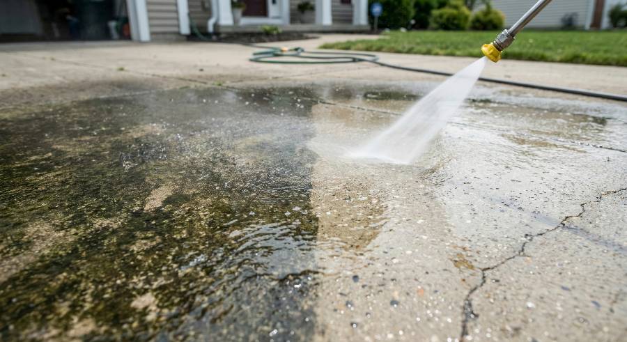 Pressure washing driveway with high-powered water spray removing dirt and algae